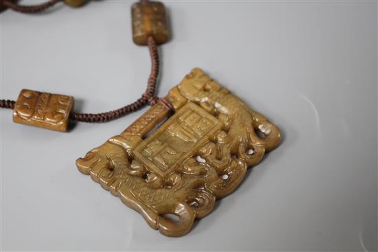 A Chinese hardstone necklace, with carved and inscribed plaque and brown fabric strung beads, plaque 6 x 4.5cm, rectangular beads 2cm a